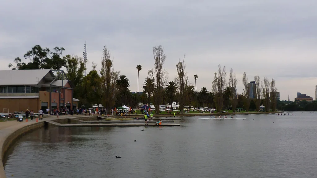Panoramic view across Albert Park Lake showing rowing boats on the water and parkland surroundings near the venue.