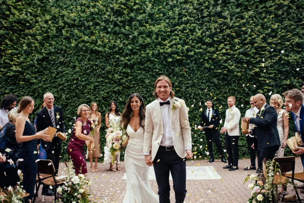 Bride and groom walking hand-in-hand after an outdoor wedding ceremony in front of the living green wall at Butler Lane.