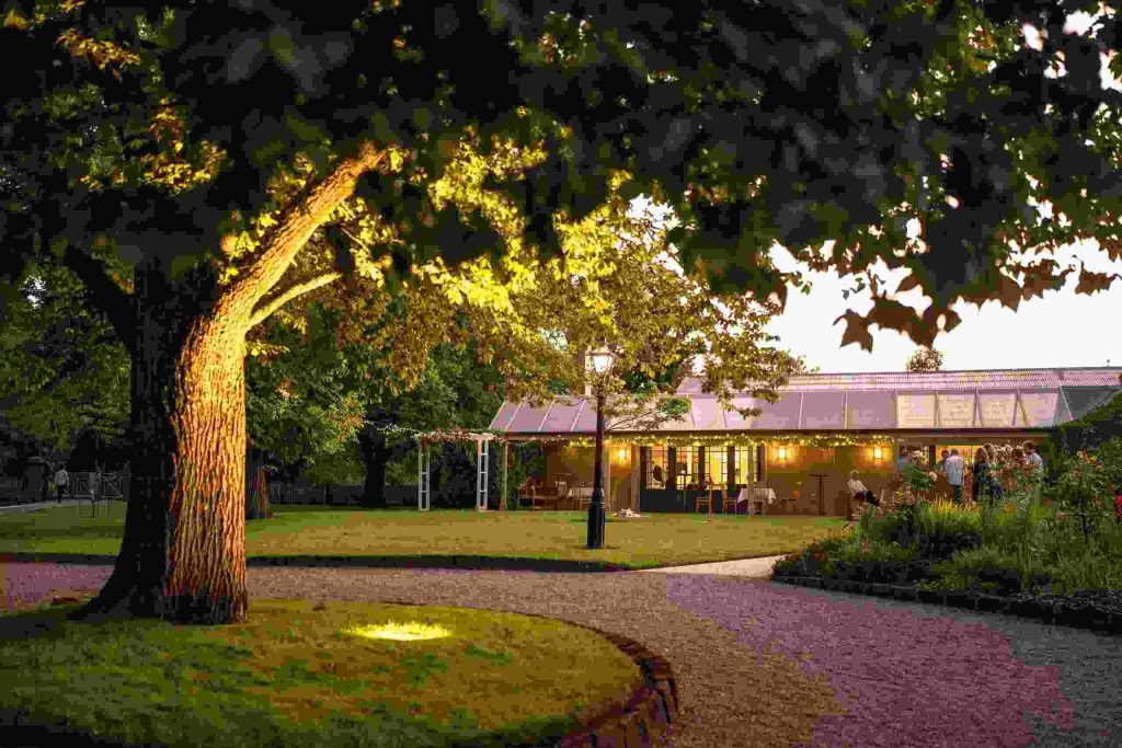 Warmly lit Garden Room pavilion and manicured lawn framed by mature trees at dusk at Narmbool estate in Elaine.