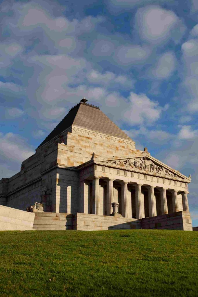 Iconic classical stone facade and Doric columns of the Shrine of Remembrance in Melbourne against a blue sky.