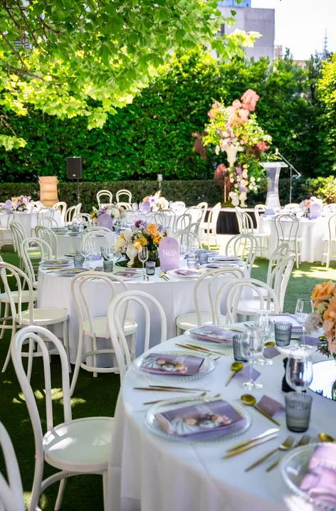 Outdoor garden reception setup with white bentwood chairs and floral table arrangements in the Hellenic Museum courtyard.