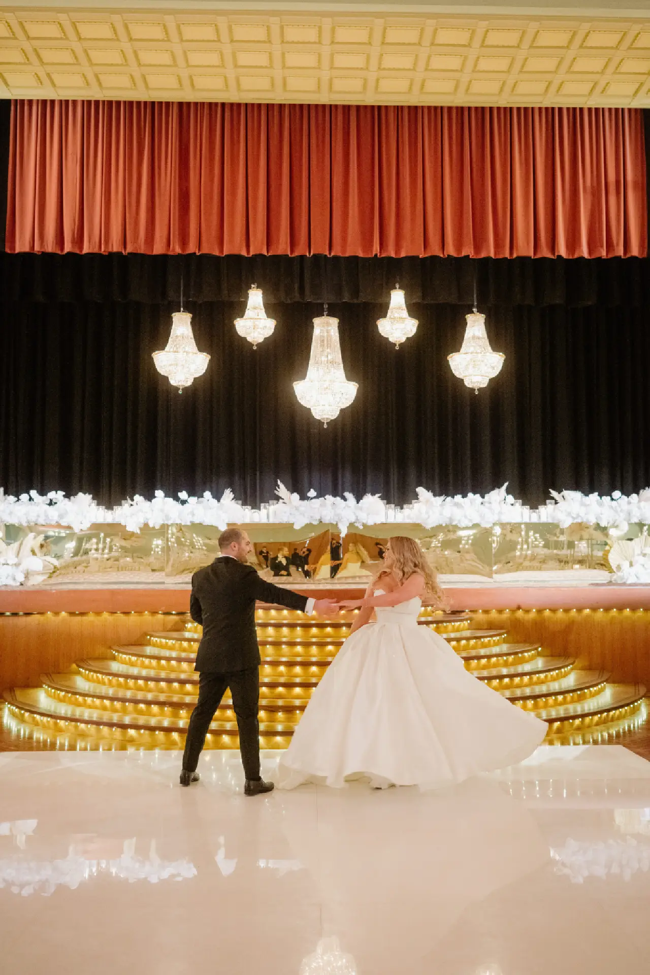 Newlyweds standing in front of the illuminated stage and Art Deco chandeliers at The Centre Ivanhoe.