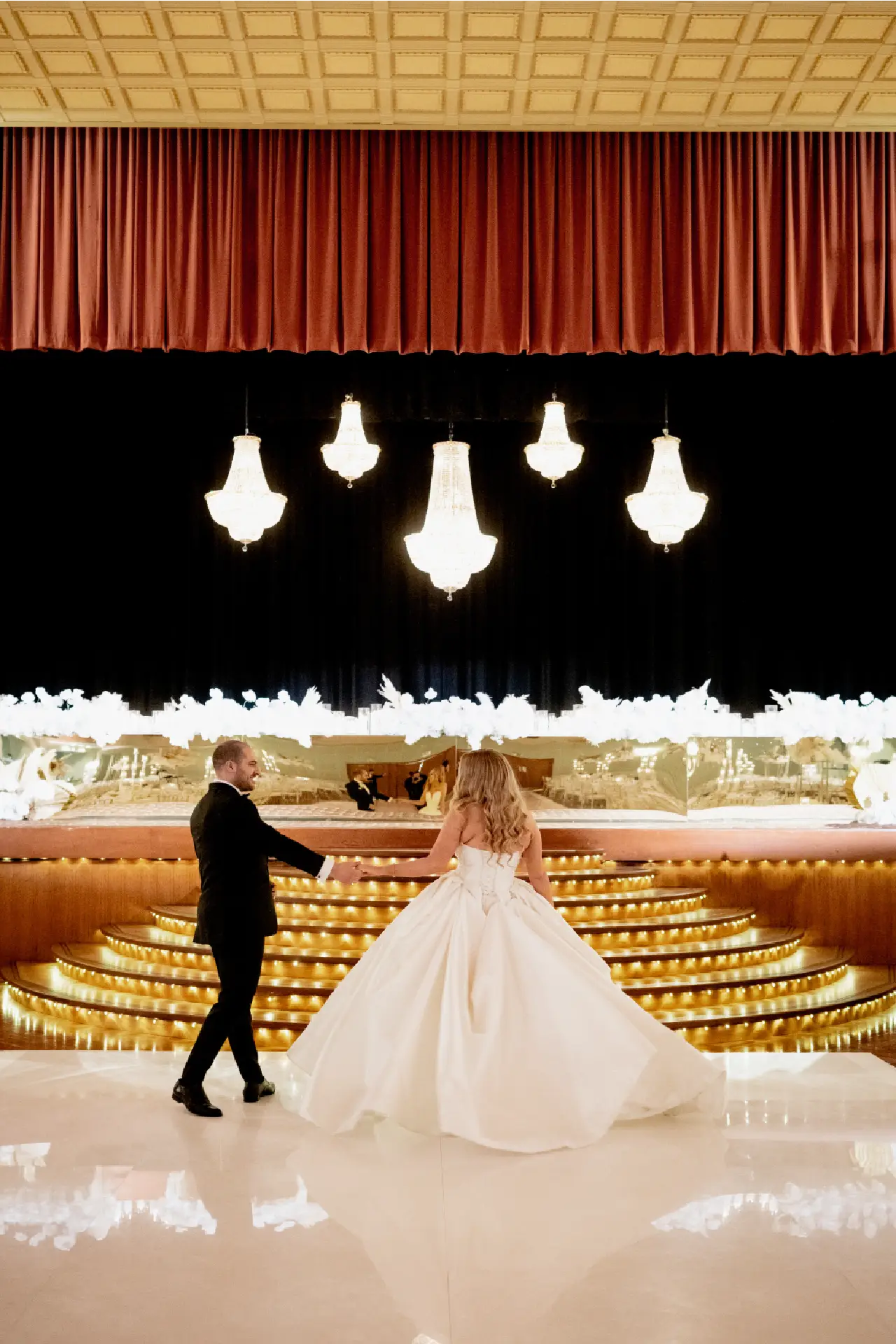 Bride and groom standing on the parquetry dance floor beneath glowing Art Deco chandeliers at The Centre Ivanhoe.