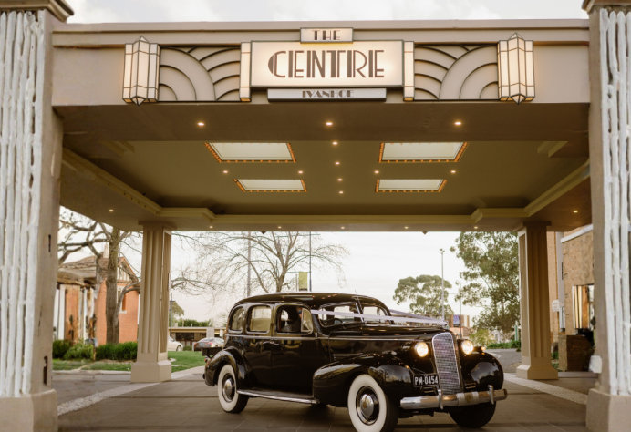 Vintage classic car parked beneath the illuminated Art Deco entrance porte-cochère at The Centre Ivanhoe venue.