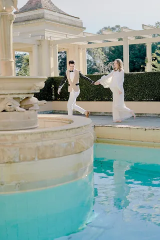 Couple in formal event attire walking along the turquoise swimming pool terrace at Rippon Lea Estate.