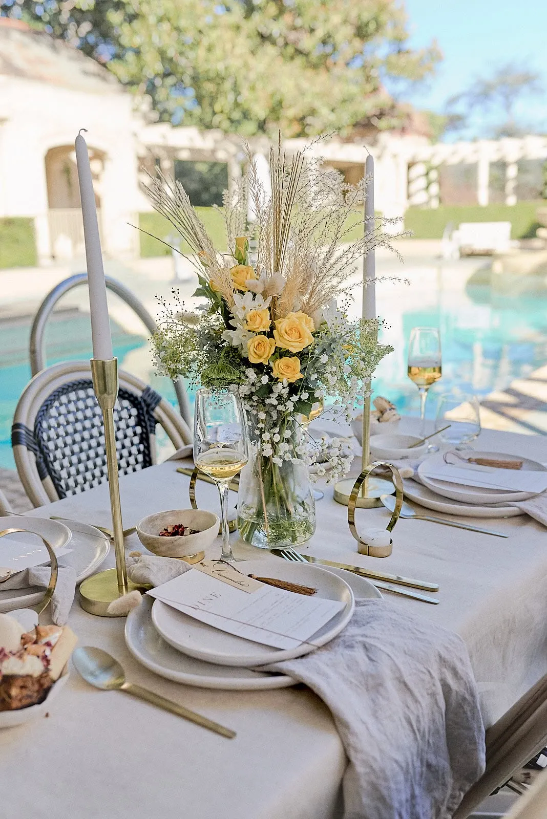 Elegant outdoor banquet dining table setting with gold cutlery and yellow floral centerpiece at Rippon Lea Estate poolside.